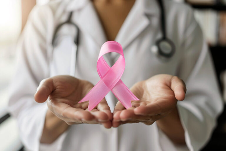 Profissional de saúde com mãos estendidas segura o laço cor de rosa, símbolo do Outubro Rosa